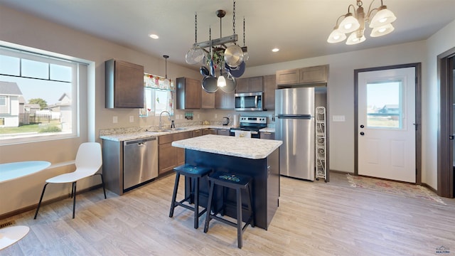 kitchen featuring decorative light fixtures, light wood-type flooring, appliances with stainless steel finishes, a notable chandelier, and a kitchen island