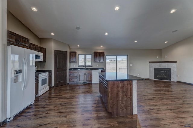 kitchen with a fireplace, white appliances, a kitchen island, sink, and dark hardwood / wood-style floors