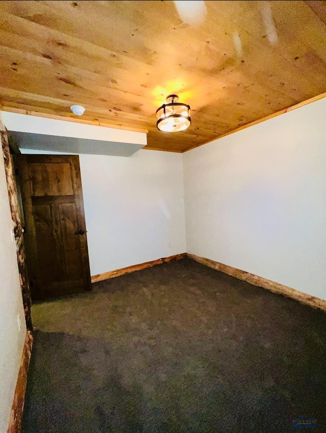 empty room featuring dark carpet, baseboards, and wooden ceiling