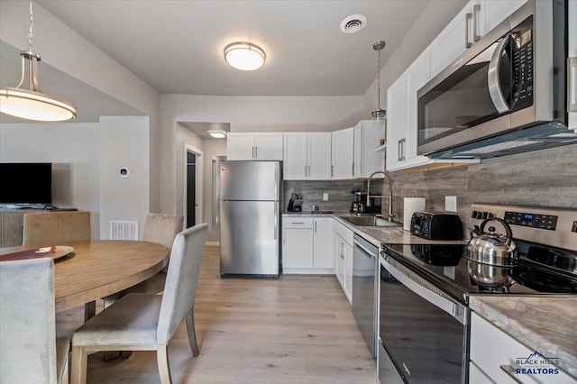 kitchen with white cabinetry, backsplash, stainless steel appliances, sink, and light hardwood / wood-style floors