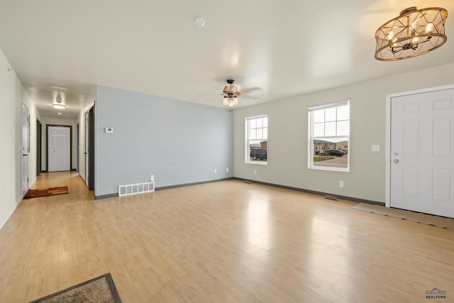 unfurnished living room with ceiling fan with notable chandelier and light hardwood / wood-style floors