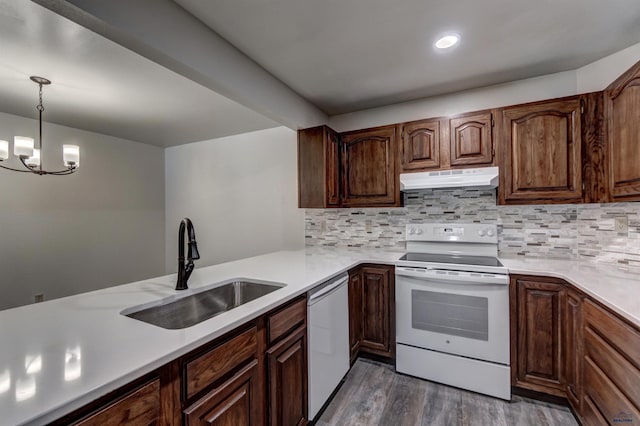 kitchen with a notable chandelier, white appliances, sink, hanging light fixtures, and dark wood-type flooring