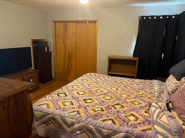 bedroom with a textured ceiling, wood-type flooring, and a closet