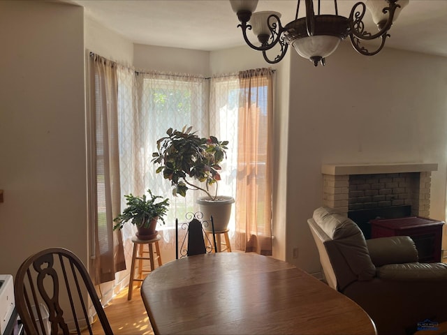 dining room with light hardwood / wood-style floors, a brick fireplace, an inviting chandelier, and a healthy amount of sunlight