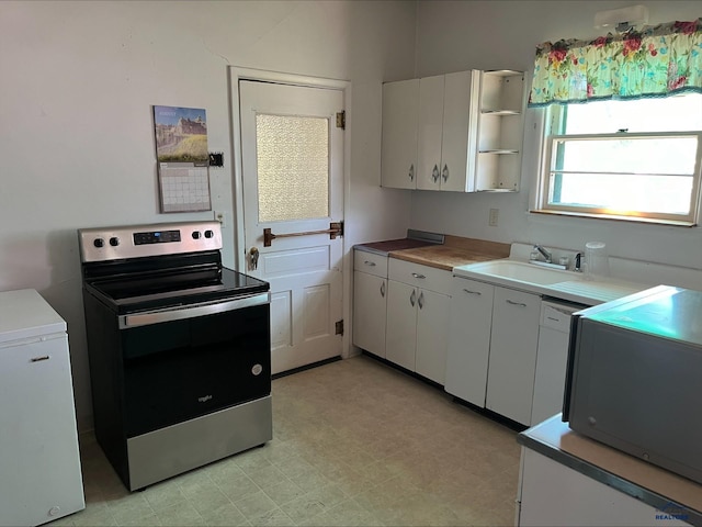 kitchen featuring white refrigerator, stainless steel electric stove, white cabinetry, and sink