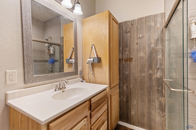 bathroom featuring a shower with shower door, wood walls, and vanity