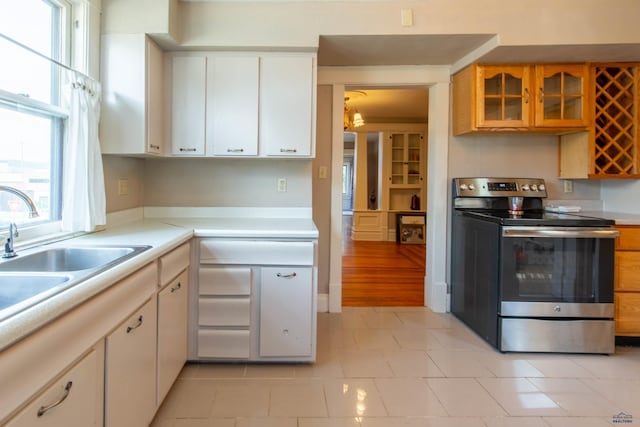 kitchen with white cabinets, electric range, light tile patterned flooring, and sink