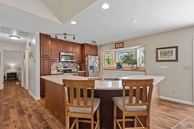 kitchen with stainless steel appliances, a textured ceiling, an island with sink, and dark hardwood / wood-style flooring