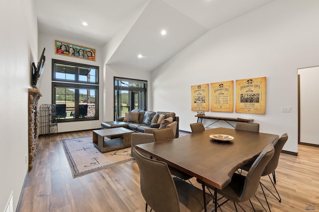 dining area with light wood-type flooring, a stone fireplace, and high vaulted ceiling