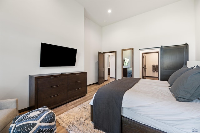 bedroom featuring light hardwood / wood-style flooring, a barn door, and high vaulted ceiling