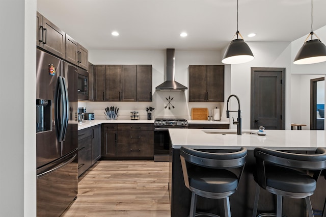 kitchen featuring wall chimney exhaust hood, sink, stainless steel appliances, and decorative light fixtures