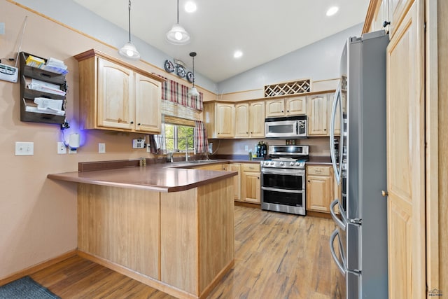 kitchen with pendant lighting, lofted ceiling, kitchen peninsula, appliances with stainless steel finishes, and light hardwood / wood-style floors