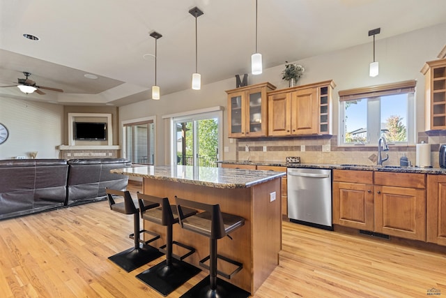 kitchen featuring dark stone counters, a kitchen bar, backsplash, ceiling fan, and stainless steel dishwasher