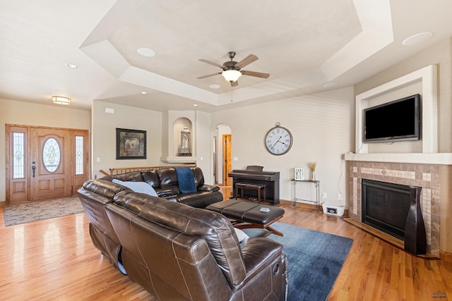 living room featuring ceiling fan, light wood-type flooring, and a tray ceiling