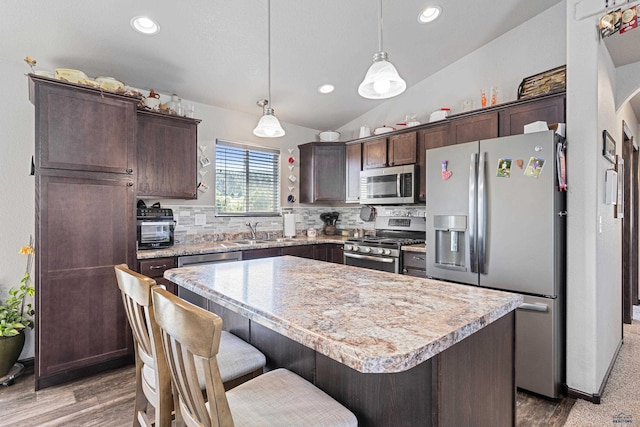 kitchen with lofted ceiling, a kitchen island, stainless steel appliances, backsplash, and dark brown cabinetry