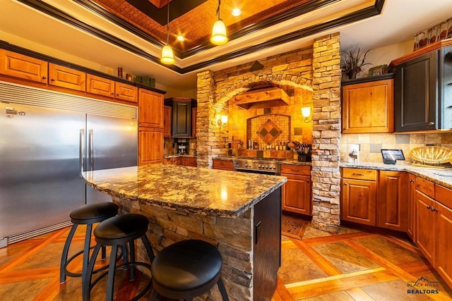 kitchen with a raised ceiling, ornamental molding, premium appliances, backsplash, and a center island