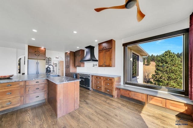 kitchen featuring sink, wall chimney range hood, hardwood / wood-style floors, and black range oven