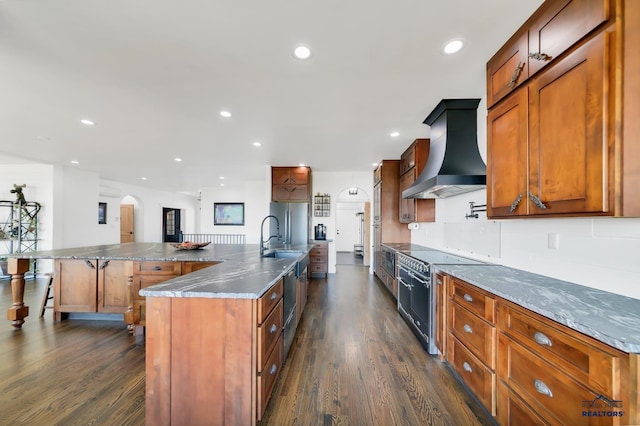 kitchen with stainless steel refrigerator, dark wood-type flooring, wall chimney range hood, a breakfast bar area, and a spacious island