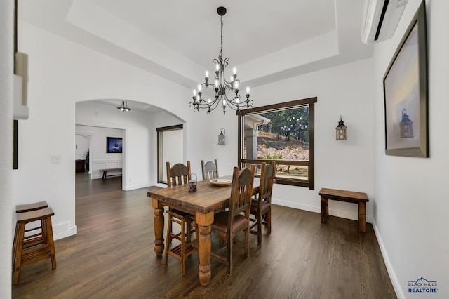 dining area with ceiling fan with notable chandelier, a tray ceiling, dark hardwood / wood-style flooring, and a wall unit AC