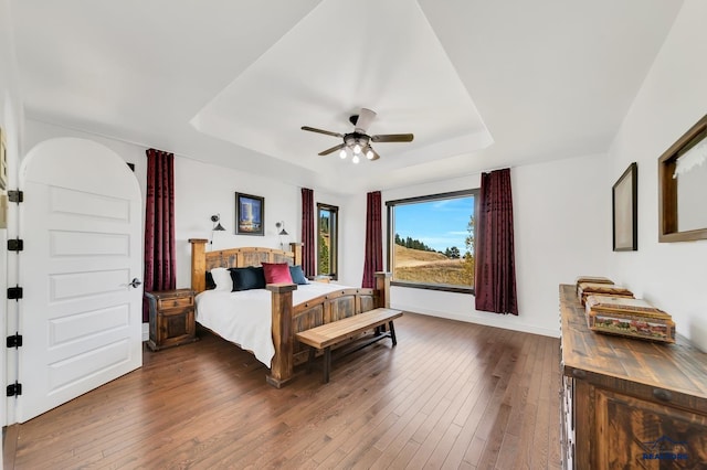 bedroom featuring ceiling fan, a raised ceiling, and dark wood-type flooring