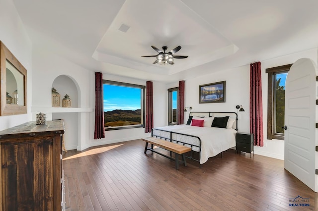 bedroom featuring a raised ceiling, dark hardwood / wood-style flooring, and ceiling fan