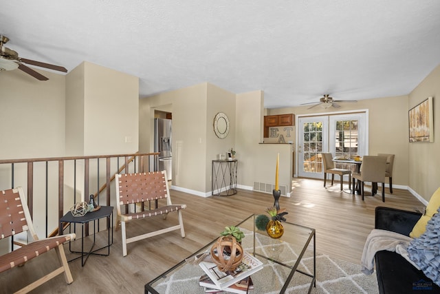 living room with light hardwood / wood-style floors, a textured ceiling, and ceiling fan