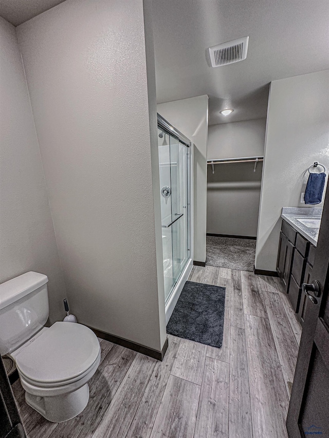 bathroom with wood-type flooring, vanity, toilet, and a shower with door