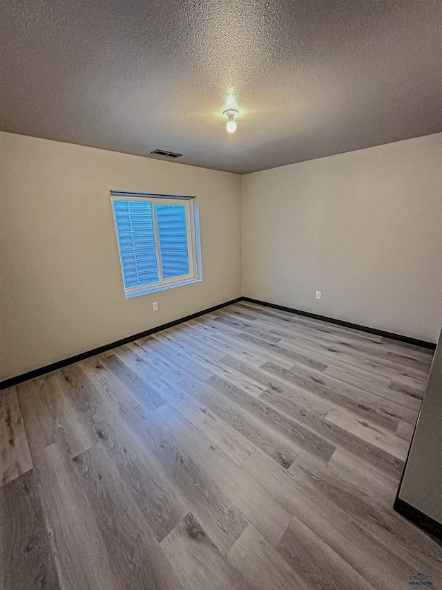 empty room featuring a textured ceiling and light hardwood / wood-style flooring