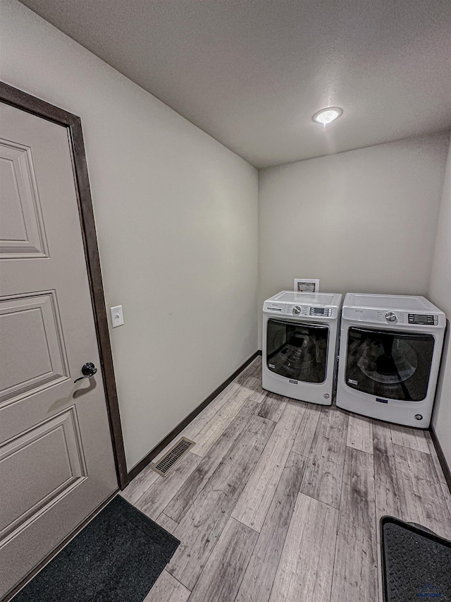 laundry area with light wood-type flooring, washing machine and clothes dryer, and a textured ceiling