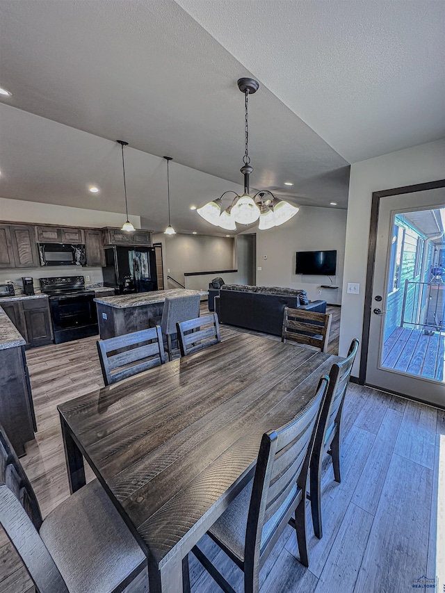 dining room with a textured ceiling, lofted ceiling, a notable chandelier, and light hardwood / wood-style flooring