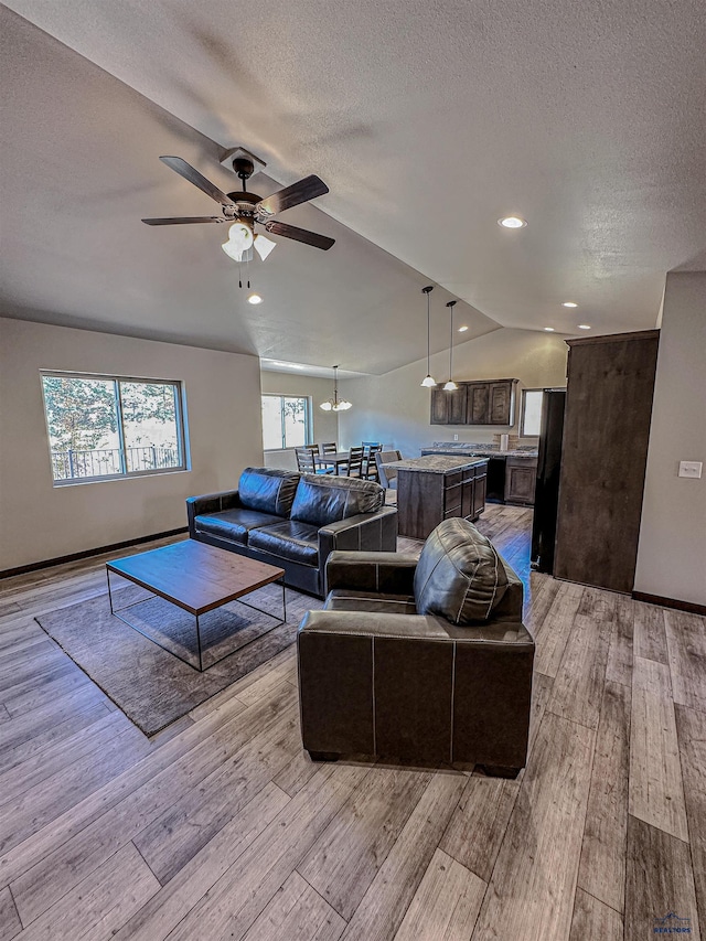 living room with ceiling fan, light wood-type flooring, lofted ceiling, and a textured ceiling