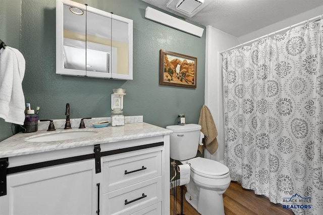 bathroom with wood finished floors, toilet, vanity, and a textured wall