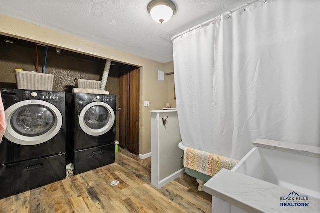 clothes washing area with independent washer and dryer, wood finished floors, a textured ceiling, and baseboards