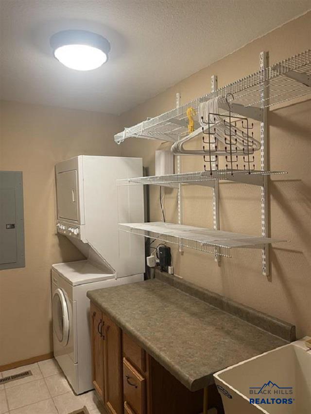 clothes washing area with cabinets, light tile patterned floors, electric panel, and stacked washer and dryer