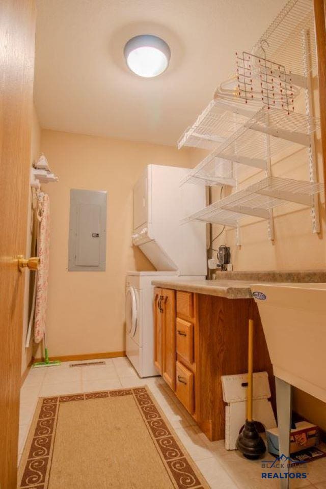 clothes washing area featuring stacked washing maching and dryer, light tile patterned floors, and electric panel