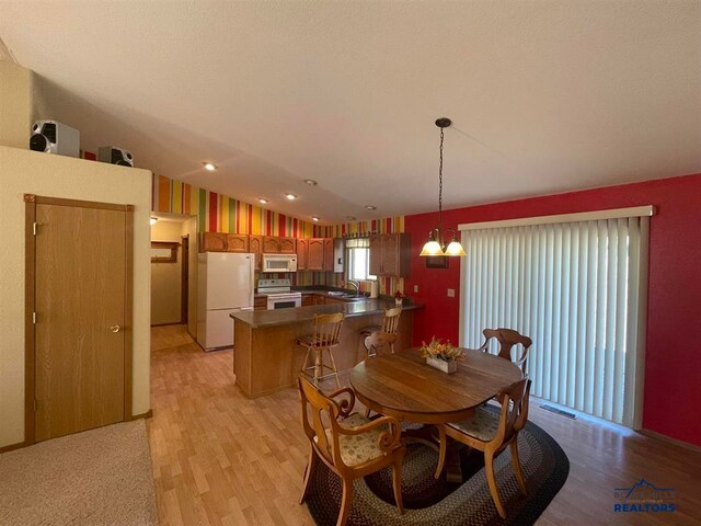 dining space featuring lofted ceiling, light wood-type flooring, sink, and an inviting chandelier