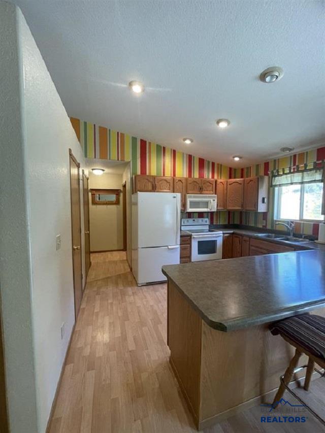 kitchen featuring light hardwood / wood-style floors, kitchen peninsula, sink, white appliances, and a textured ceiling