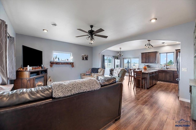 living room with dark wood-type flooring, ceiling fan with notable chandelier, and sink