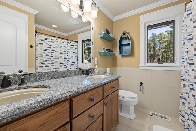 bathroom with tile patterned floors, toilet, vanity, ornamental molding, and tile walls