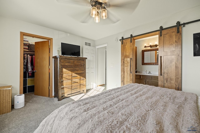 carpeted bedroom with a closet, a walk in closet, ensuite bath, sink, and ceiling fan