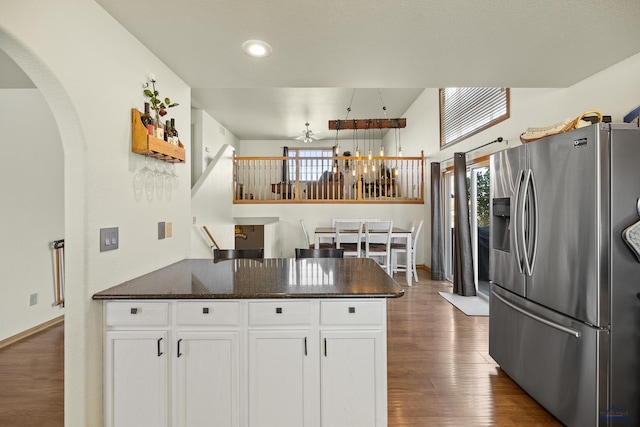 kitchen with stainless steel fridge, hanging light fixtures, white cabinetry, dark stone counters, and dark wood-type flooring