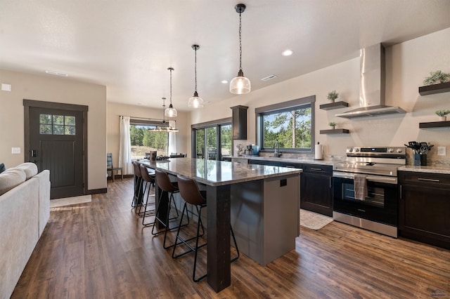 kitchen featuring stainless steel range with electric cooktop, hanging light fixtures, dark wood-type flooring, wall chimney exhaust hood, and a center island