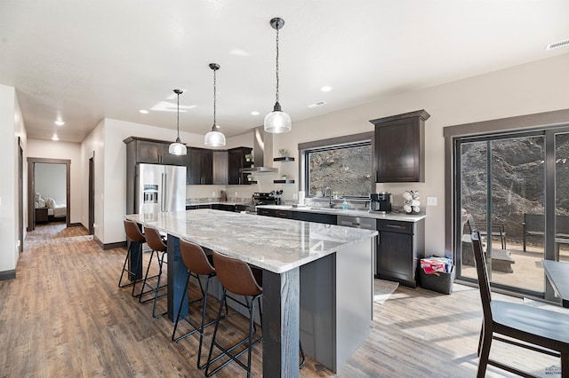 kitchen with a kitchen island, hanging light fixtures, dark brown cabinets, light wood-type flooring, and appliances with stainless steel finishes