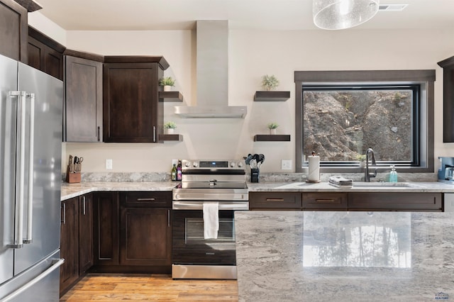 kitchen featuring wall chimney exhaust hood, stainless steel appliances, sink, light stone counters, and light hardwood / wood-style floors