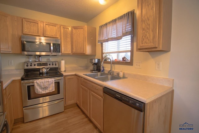 kitchen with appliances with stainless steel finishes, sink, light brown cabinetry, a textured ceiling, and light hardwood / wood-style flooring