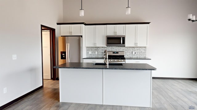 kitchen featuring a kitchen island with sink, pendant lighting, white cabinetry, and stainless steel appliances