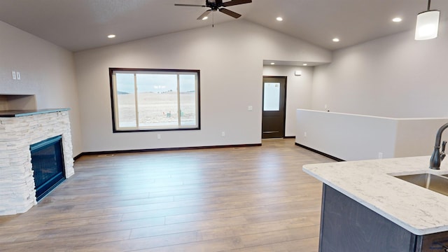 unfurnished living room featuring ceiling fan, sink, high vaulted ceiling, light hardwood / wood-style flooring, and a fireplace