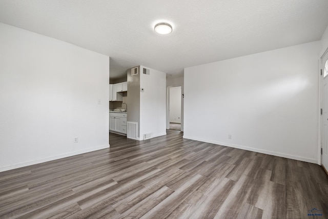 unfurnished living room with hardwood / wood-style floors, sink, and a textured ceiling