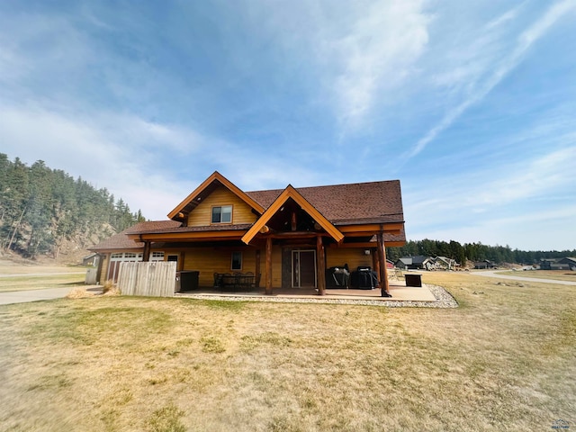 back of house featuring a shingled roof, a patio area, and a lawn