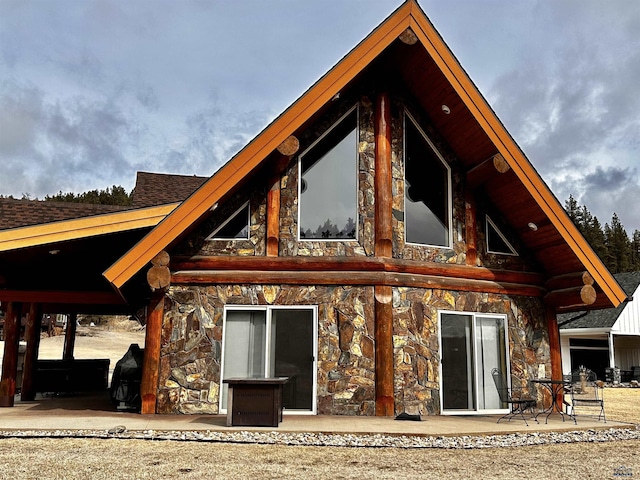 rear view of property with stone siding and a shingled roof